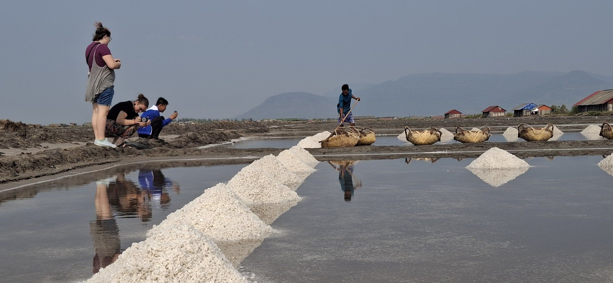 Visitors watching salt workers rake a long white ridge of harvested salt