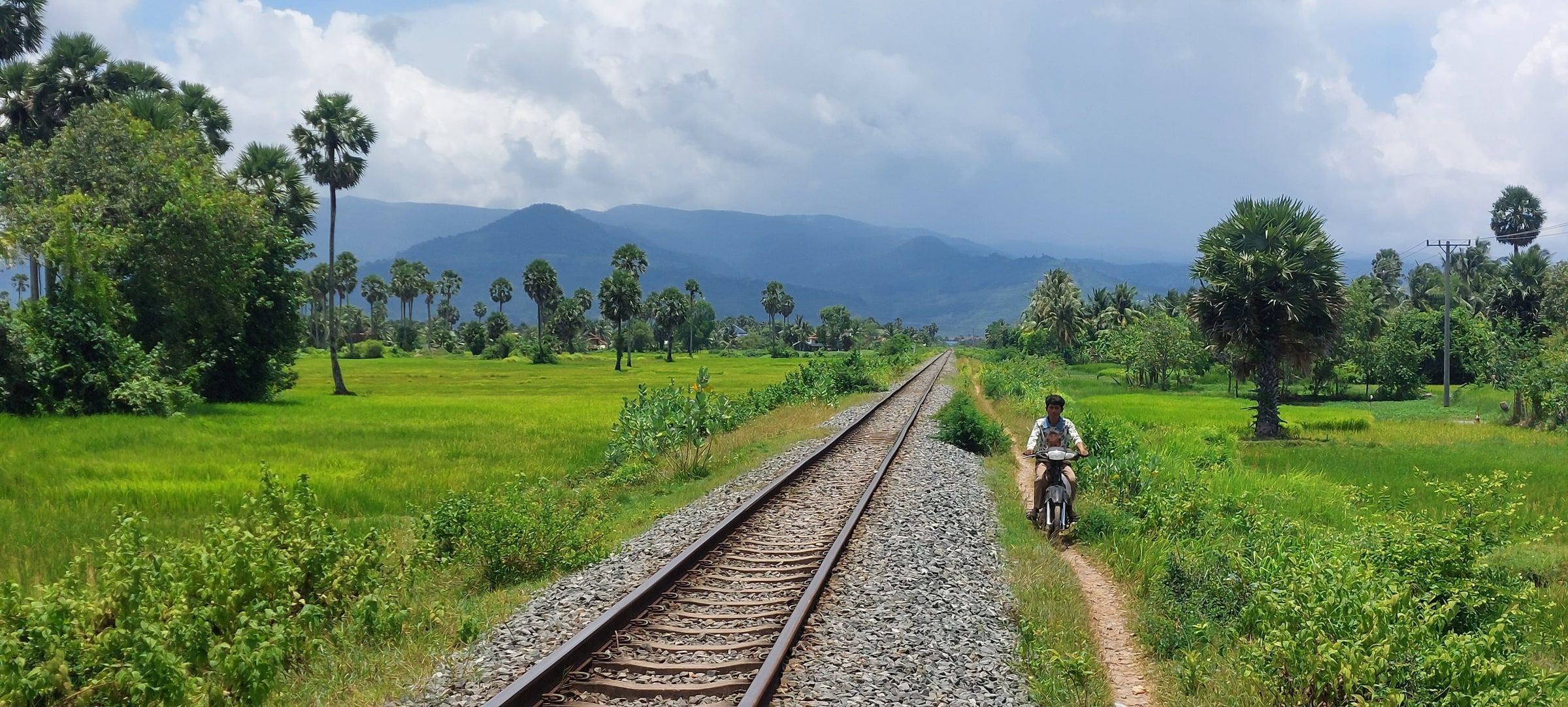 Railway tracks running straight toward the mountains, a motorbike on the path alongside